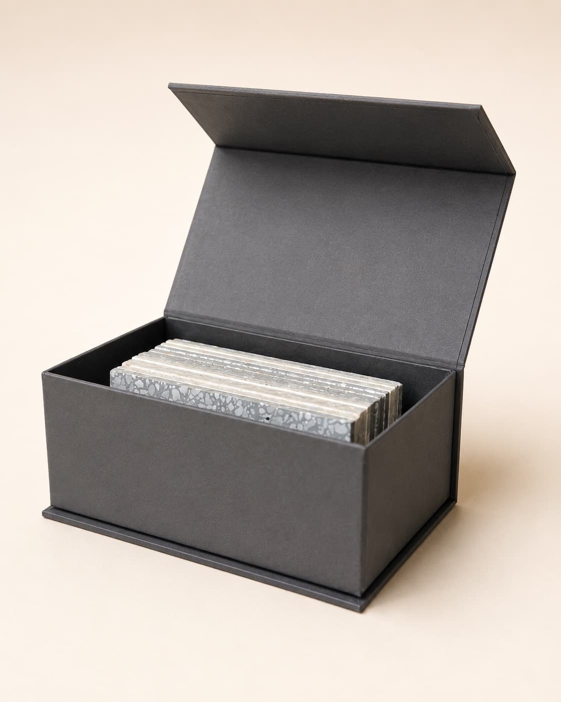 Grey magnetic-lid box open to show a stack of stone and terrazzo sample tiles standing on edge